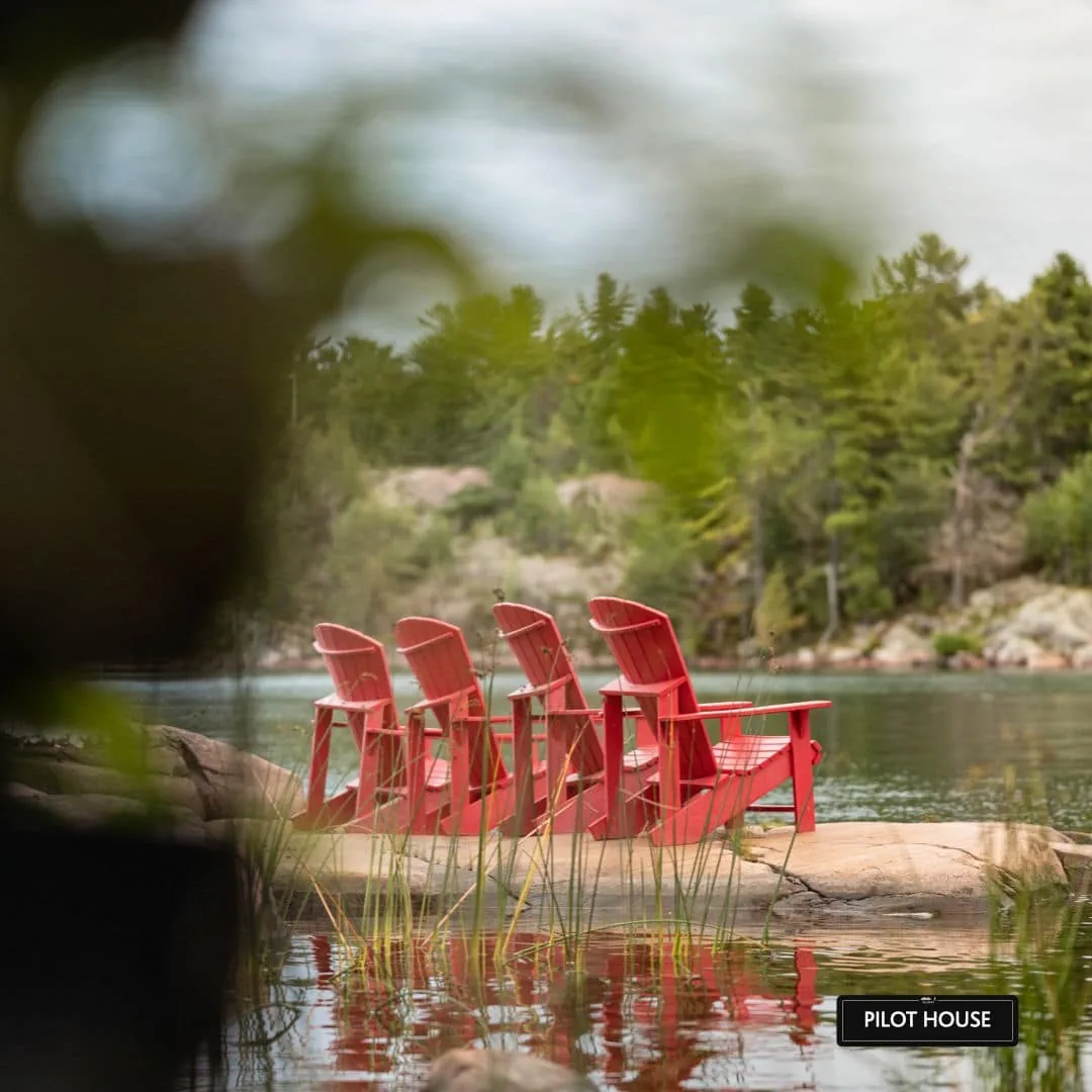 Red Adirondack chairs by the water near the Pilot House at Killarney Mountain Lodge