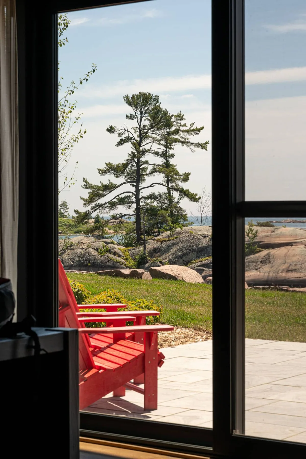 View through a cabin door toward a red chair, rocks and the channel at Killarney Mountain Lodge